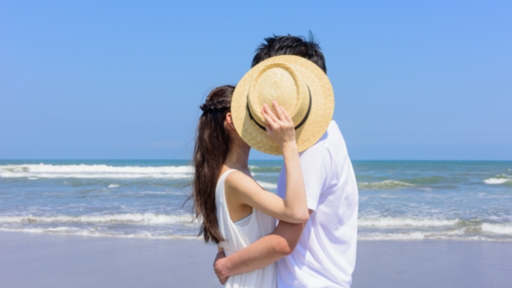 海辺で麦わら帽子を使ってキスを隠している男女